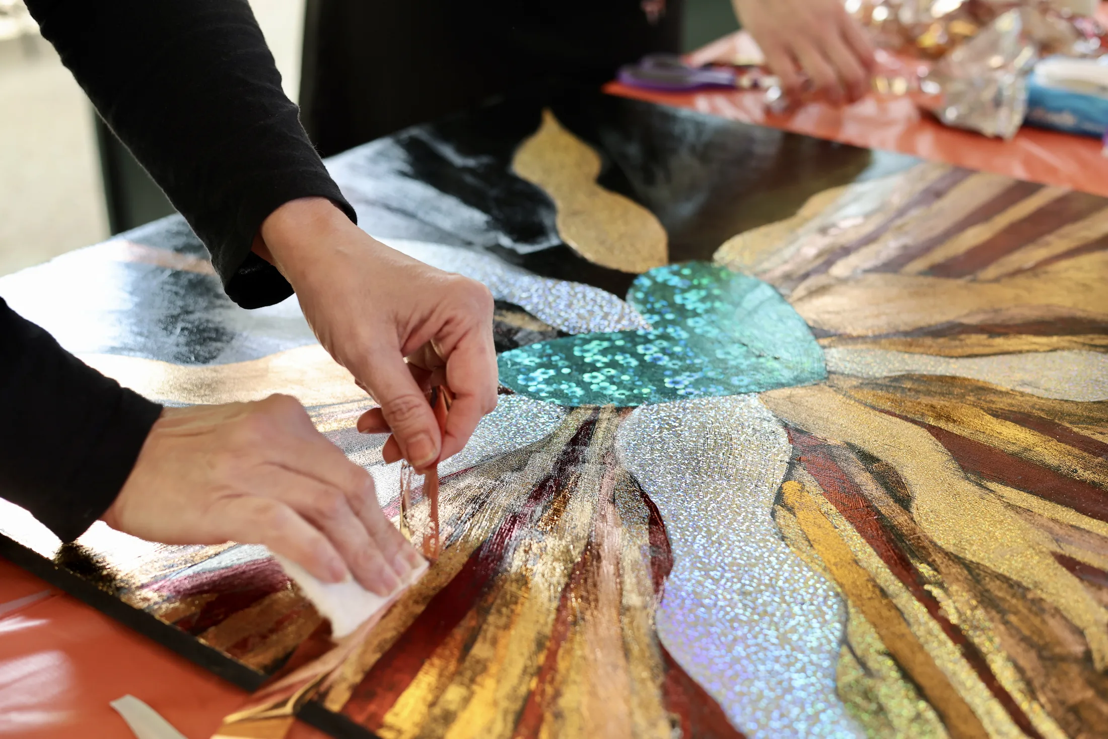 Hands working on a painted art piece at the Reclaim 13 event